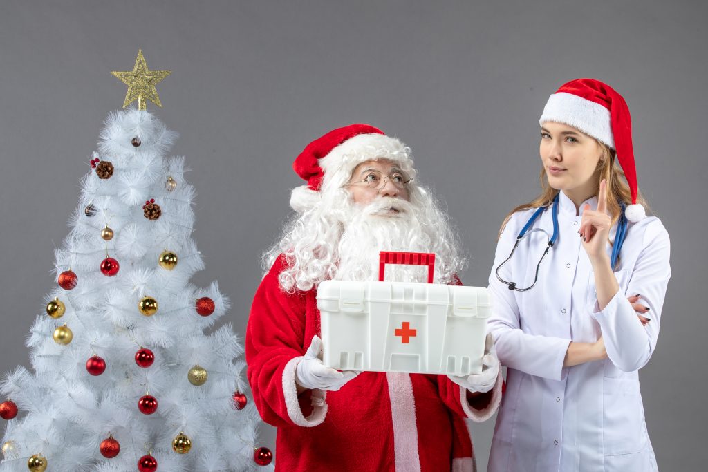 vista-frontale-di-babbo-natale-con-la-dottoressa-che-gli-ha-dato-il-kit-di-pronto-soccorso-sul-muro-grigio